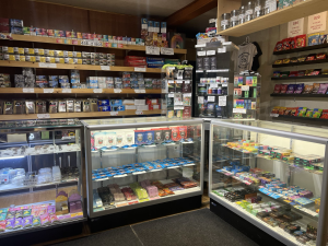 Cannabis dispensary interior with glass display cases showing edibles, vapes, and cigarettes on wood shelving in Oka, Quebec.